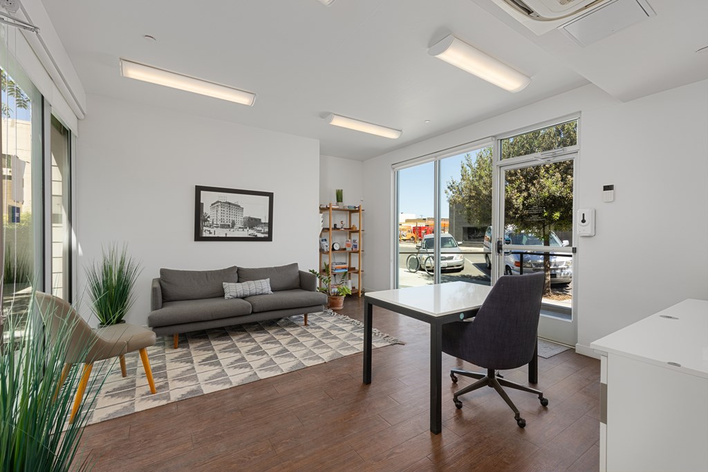 A modern office space with a grey sofa, a black chair, and a framed picture on the wall.